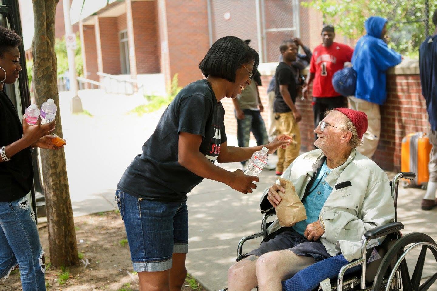 A Communities In Action volunteer handing water and a meal to a neighbor in a wheelchair